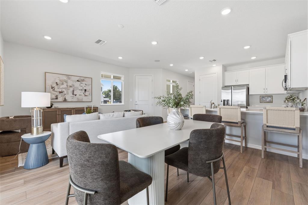 An open-concept living and dining area features white cabinetry, wood-look flooring, and modern furniture — 11363 BRILEY MAY WAY, RIVERVIEW, FL