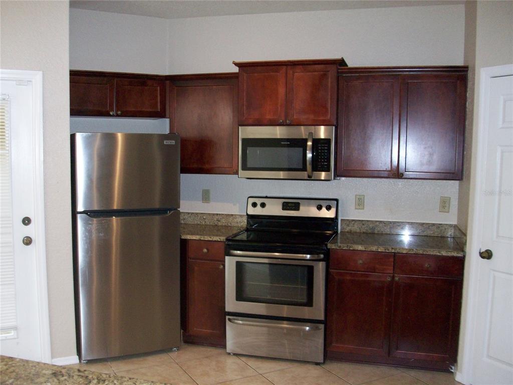A kitchen features dark wood cabinets, stainless steel appliances, and granite countertops — 143 VILLA DI ESTE TERRACE UNIT 205, LAKE MARY, FL