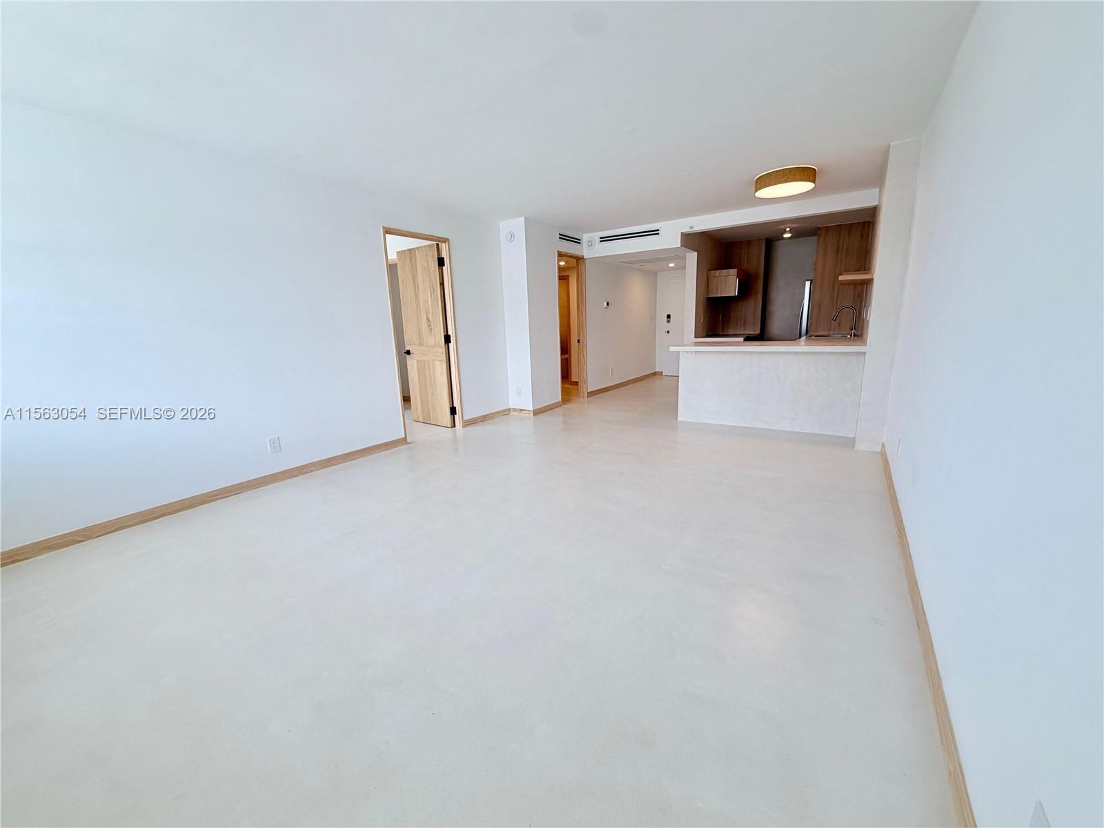 An open-concept living area features white walls, light flooring, and a kitchen with wood cabinetry — 100 Lincoln Rd # 1241, Miami Beach FL 33139, MIAMI BEACH, FL