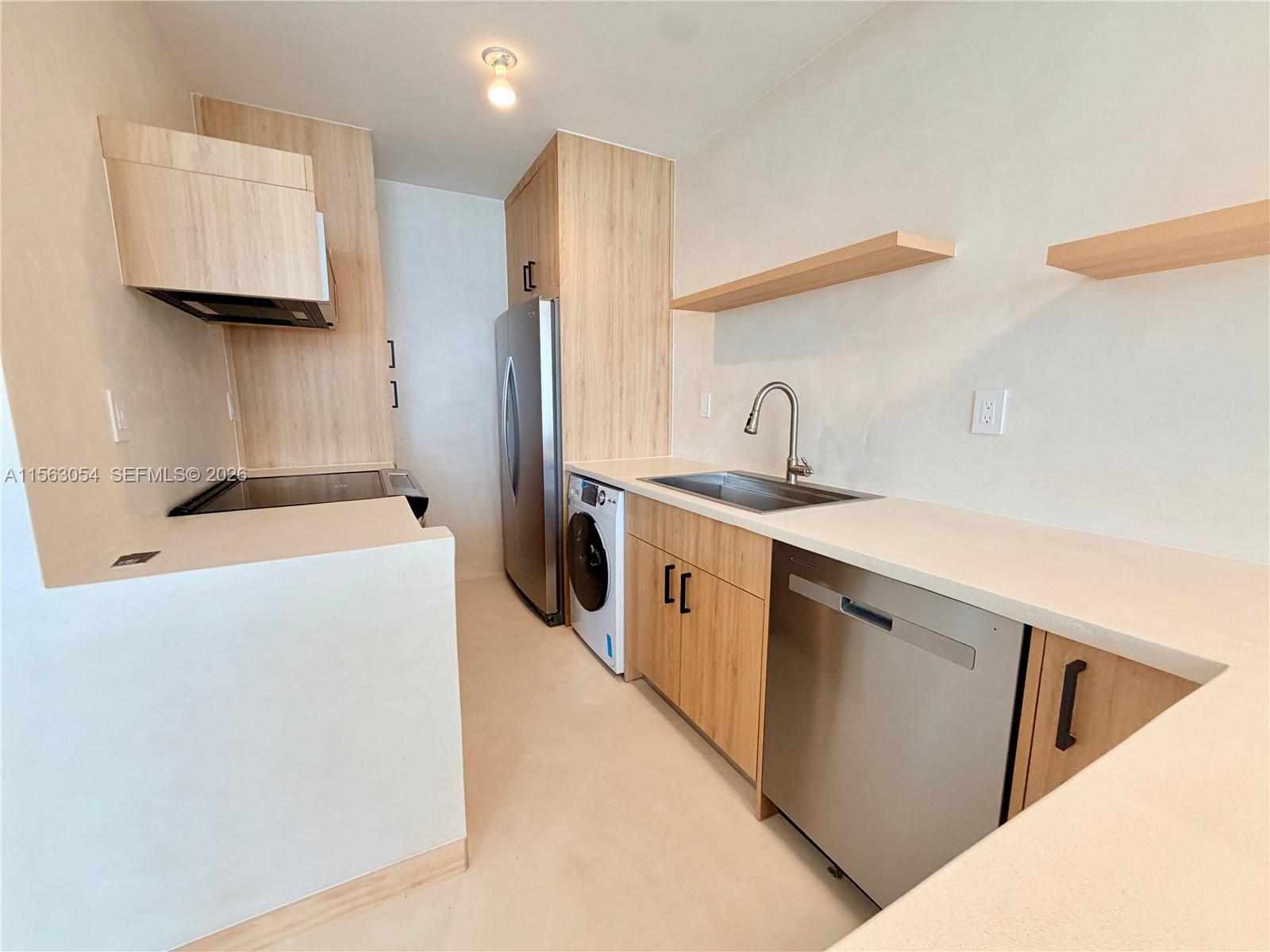 A modern kitchen features light wood cabinetry, stainless steel appliances, and a built-in laundry unit — 100 Lincoln Rd # 1241, Miami Beach FL 33139, MIAMI BEACH, FL