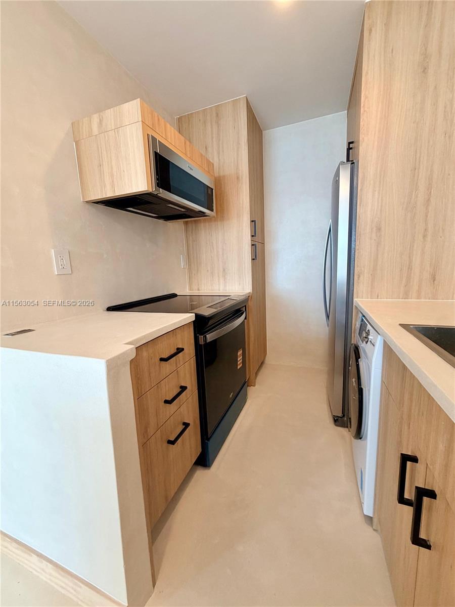 A narrow kitchen features light wood cabinets, stainless steel appliances, and a white countertop — 100 Lincoln Rd # 1241, Miami Beach FL 33139, MIAMI BEACH, FL