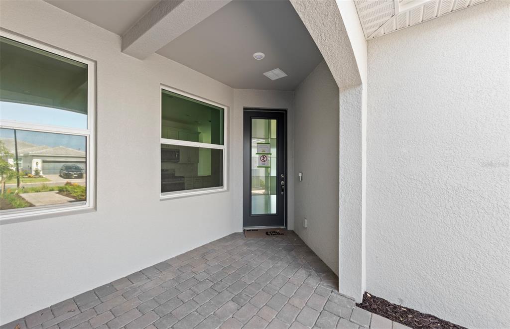 A covered entryway features a paved floor, a dark-framed glass door, and a large window — 27112 CLAM SHELL COURT, ENGLEWOOD, FL