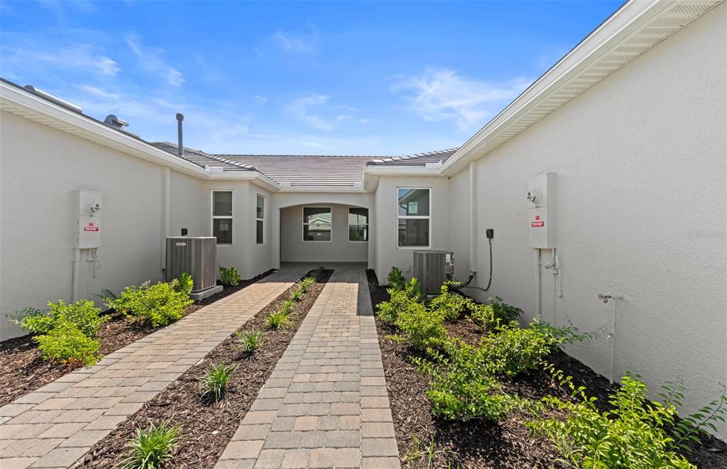 A paved walkway leads to a recessed entryway between two wings of a stucco house — 27112 CLAM SHELL COURT, ENGLEWOOD, FL