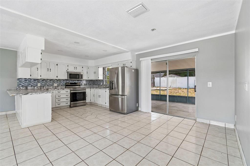 A kitchen with white cabinets, stainless steel appliances, and tiled floors leads to a patio — 1719 JULIAN LANE DRIVE, TAMPA, FL