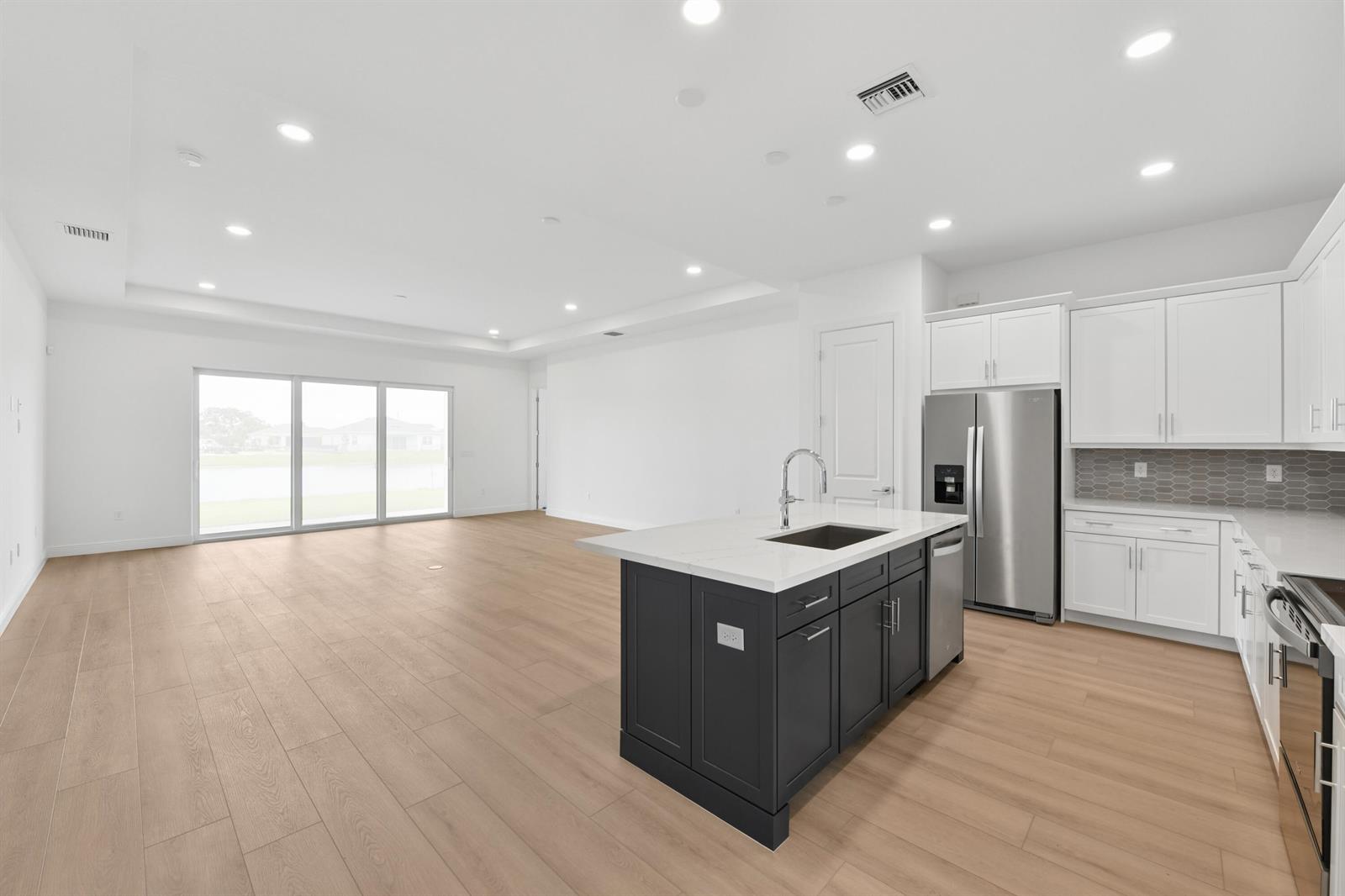 A modern kitchen with a dark island and white cabinets opens into a spacious living area — 2850 68th Street, Vero Beach FL 32967, VERO BEACH, FL