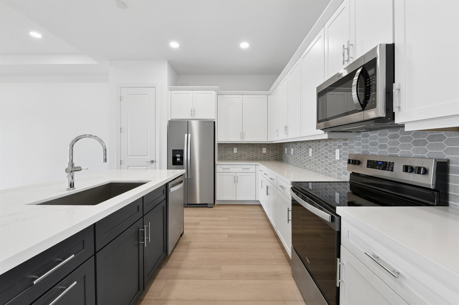 A modern kitchen features white upper cabinets, dark lower island cabinets, and stainless steel appliances — 2850 68th Street, Vero Beach FL 32967, VERO BEACH, FL