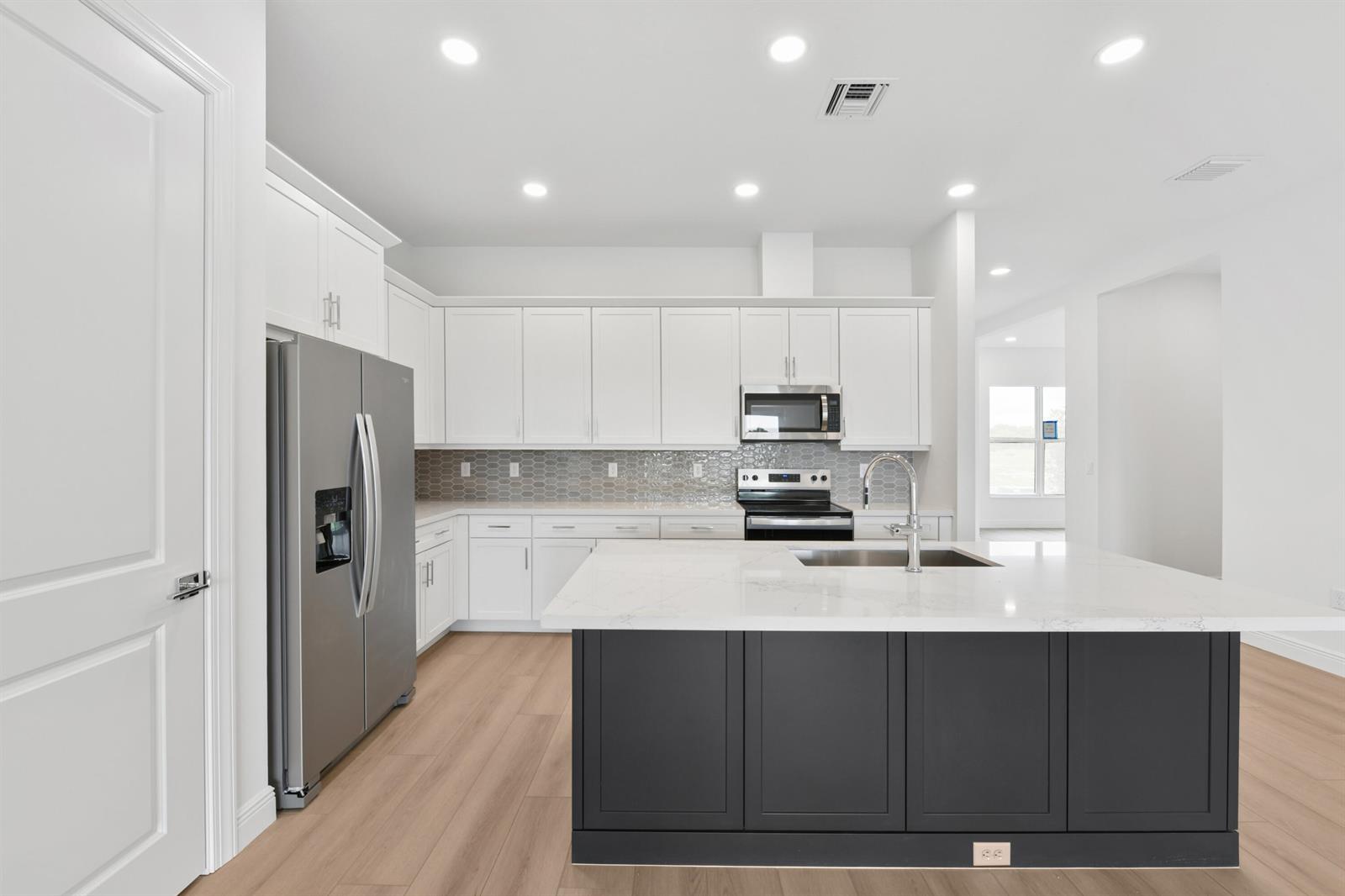 A modern kitchen features white upper cabinets, a dark gray island, and stainless steel appliances — 2850 68th Street, Vero Beach FL 32967, VERO BEACH, FL