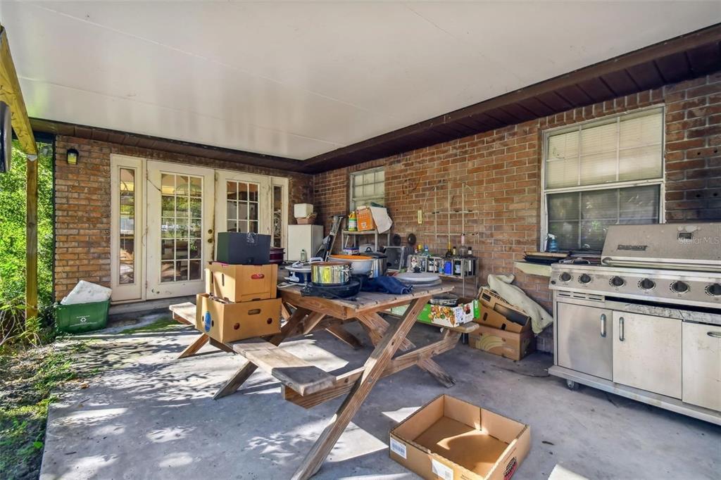 A covered brick patio features a wooden picnic table, a stainless steel grill, and boxes — 10901 MCMULLEN LOOP, RIVERVIEW, FL