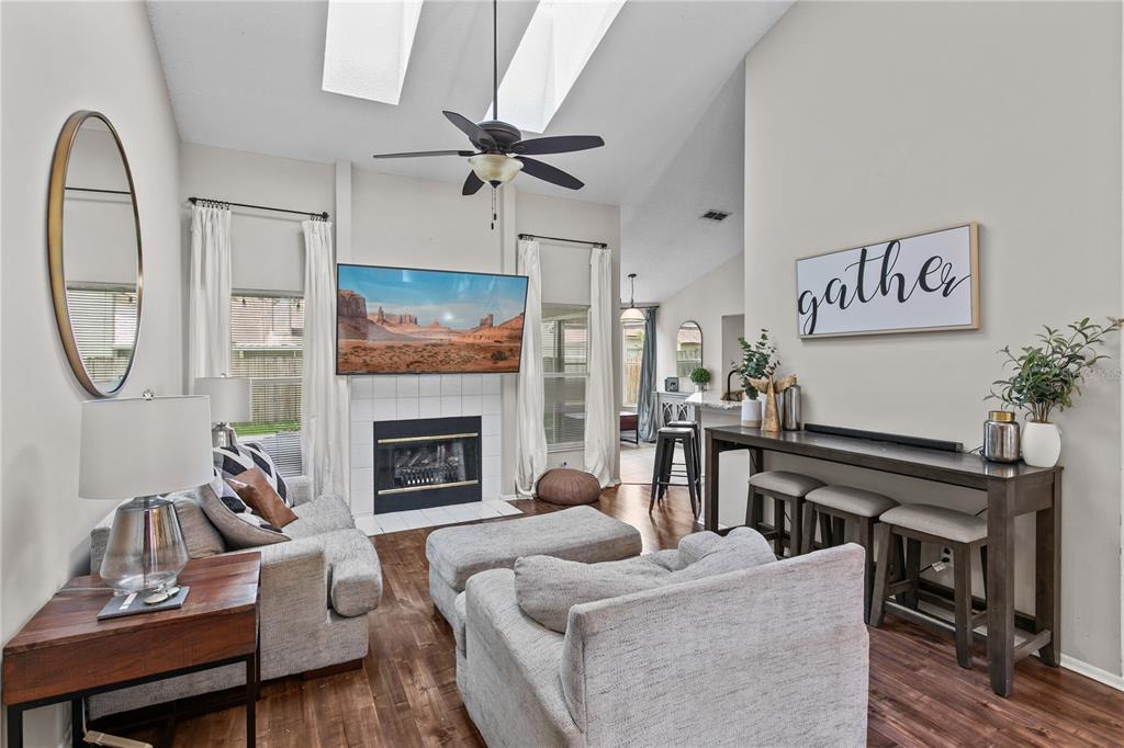 A living room features a fireplace with a mounted television, vaulted ceilings, and wood flooring — 1322 AMERICAN ELM DRIVE, ALTAMONTE SPRINGS, FL