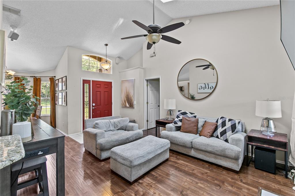 A living room features vaulted ceilings, wood-look flooring, a red front door, and gray furniture — 1322 AMERICAN ELM DRIVE, ALTAMONTE SPRINGS, FL