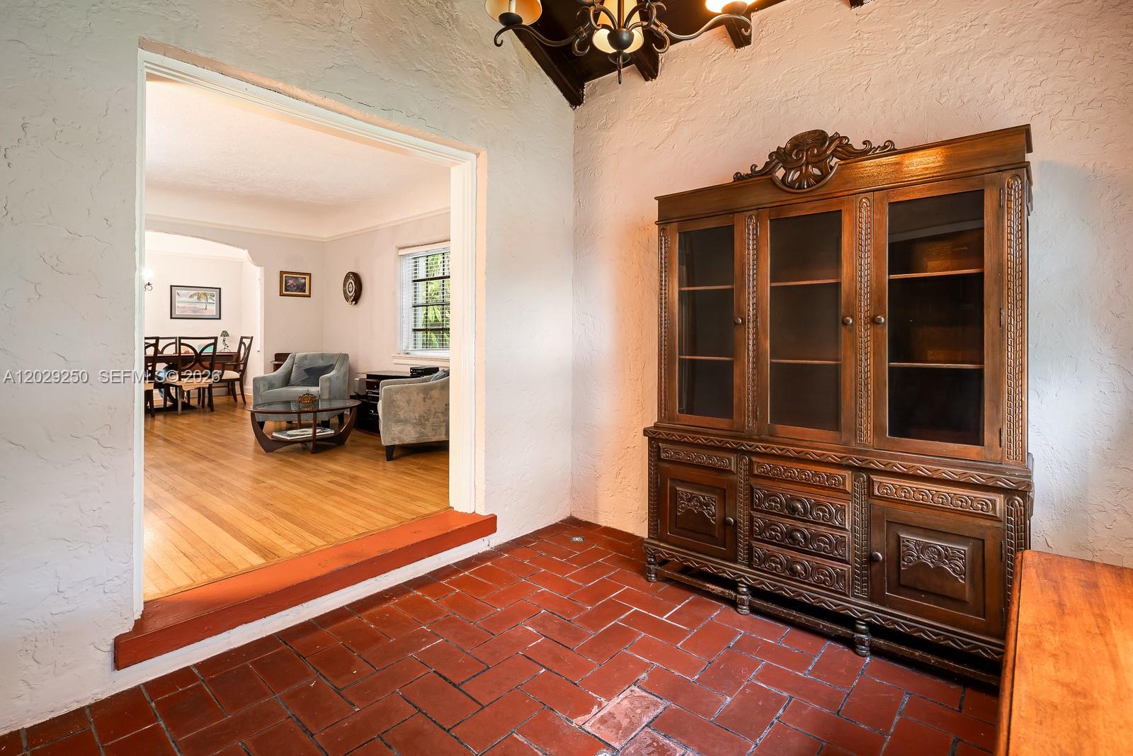 A tiled entryway with a wooden hutch leads into a living room with hardwood floors — 732 Majorca Ave, Coral Gables FL 33134, CORAL GABLES, FL