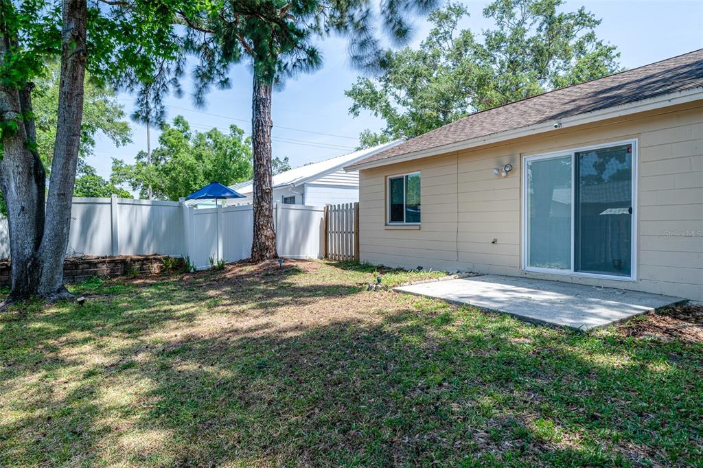A backyard features a concrete patio, a sliding glass door, and a white privacy fence — 6805 S GABRIELLE STREET, TAMPA, FL