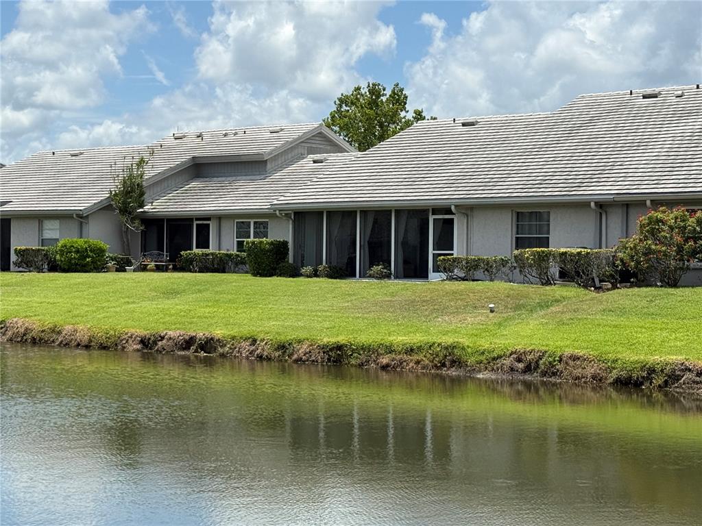 A view of the back of a residential building with a screened patio facing a pond — 5371 CRESTLAKE BOULEVARD UNIT 68, SARASOTA, FL