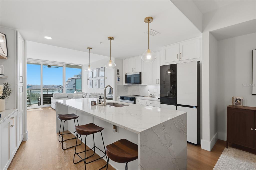 A modern kitchen features a marble waterfall island, white cabinetry, and a view of ships — 912 CHANNELSIDE DRIVE UNIT 2503, TAMPA, FL