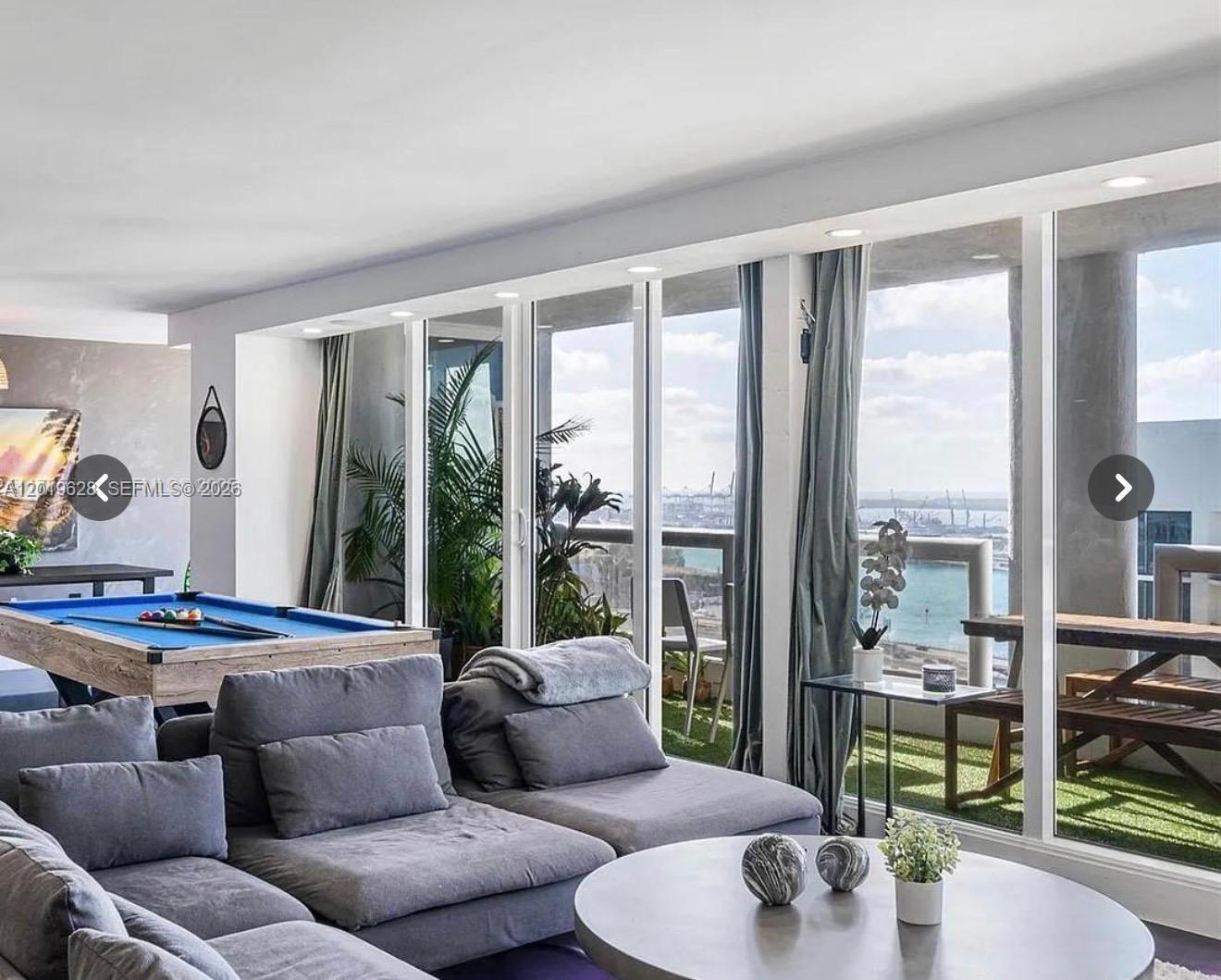 A living room with a pool table, gray sectional sofa, and a balcony overlooking water — 1717 N Bayshore Dr # 3545, Miami FL 33132, MIAMI, FL