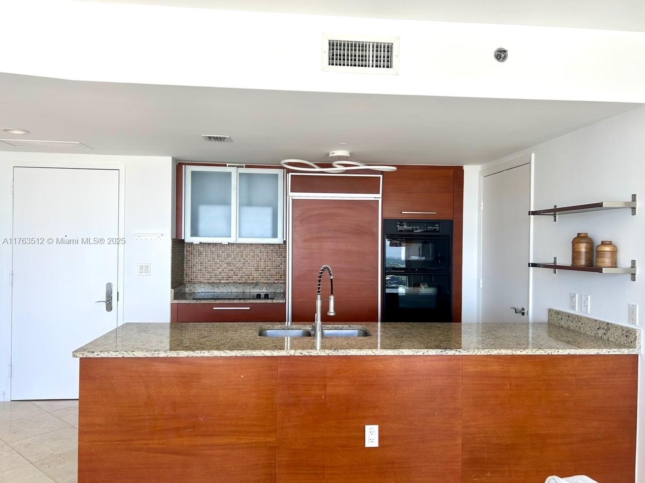 A kitchen features wood cabinetry, a granite island countertop, and built-in stainless steel appliances — 1830 S Ocean Dr # 3707, Hallandale Beach FL 33009, HALLANDALE BEACH, FL