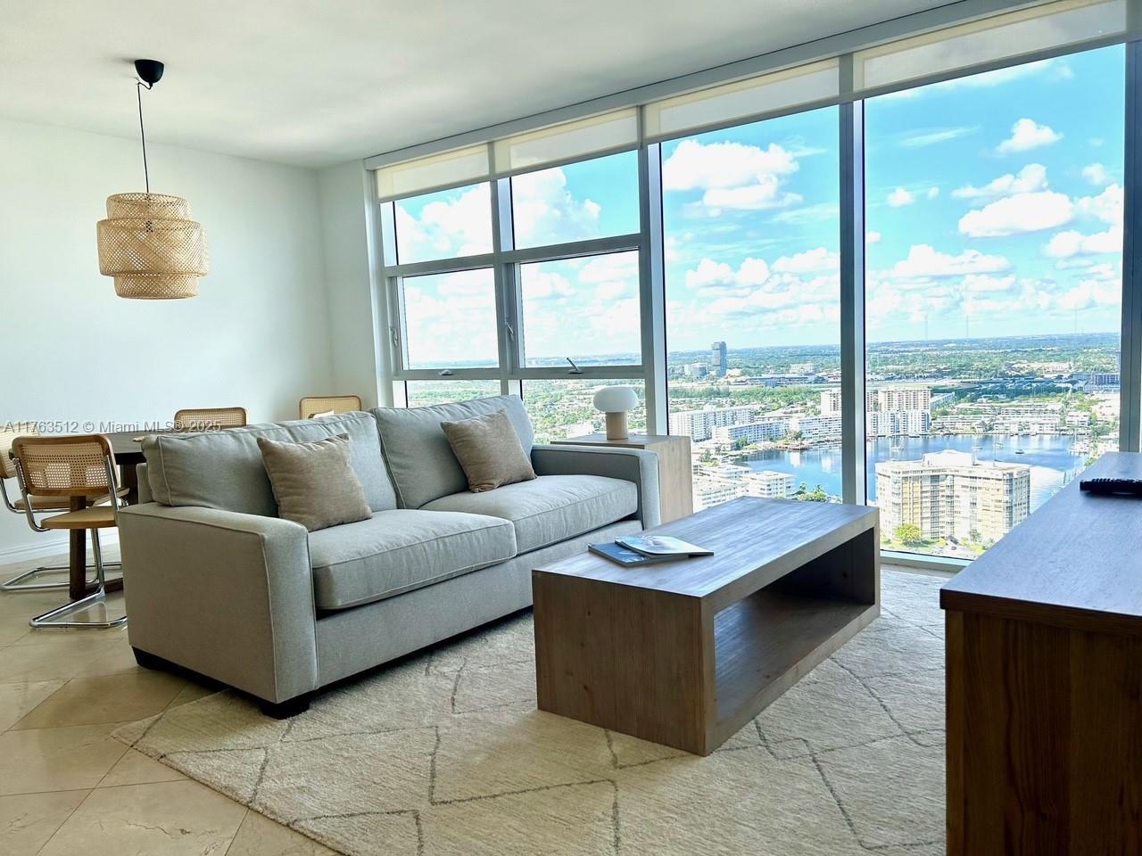 A living room features a grey sofa, wooden coffee table, and floor-to-ceiling windows overlooking water — 1830 S Ocean Dr # 3707, Hallandale Beach FL 33009, HALLANDALE BEACH, FL