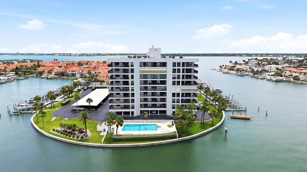 An aerial view shows a multi-story apartment building situated on a small island with a pool — 1651 SAND KEY ESTATES COURT UNIT 31, CLEARWATER, FL