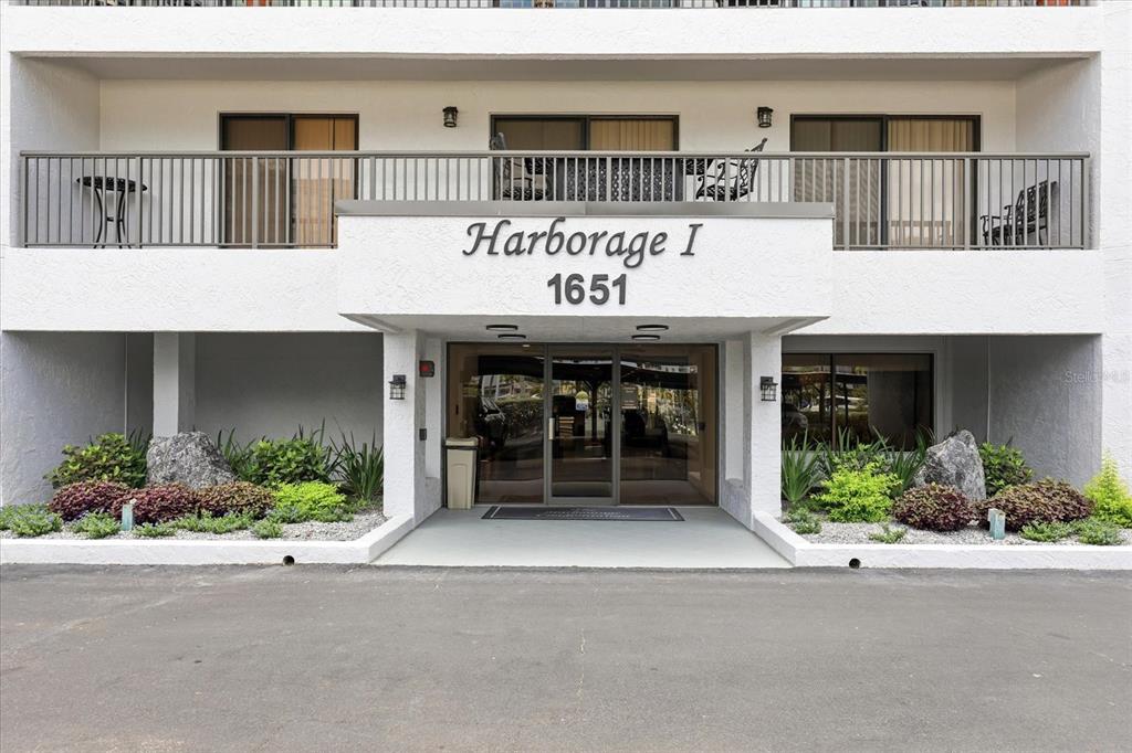 The exterior of a multi-story building entrance features a sign reading Harborage I 1651 — 1651 SAND KEY ESTATES COURT UNIT 31, CLEARWATER, FL