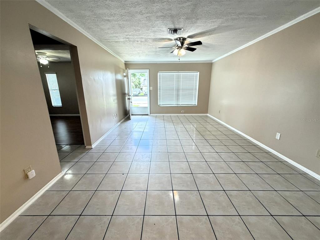 An empty room features light-colored tile flooring, beige walls, a ceiling fan, and a door — 8103 PUFFIN DRIVE, ORLANDO, FL