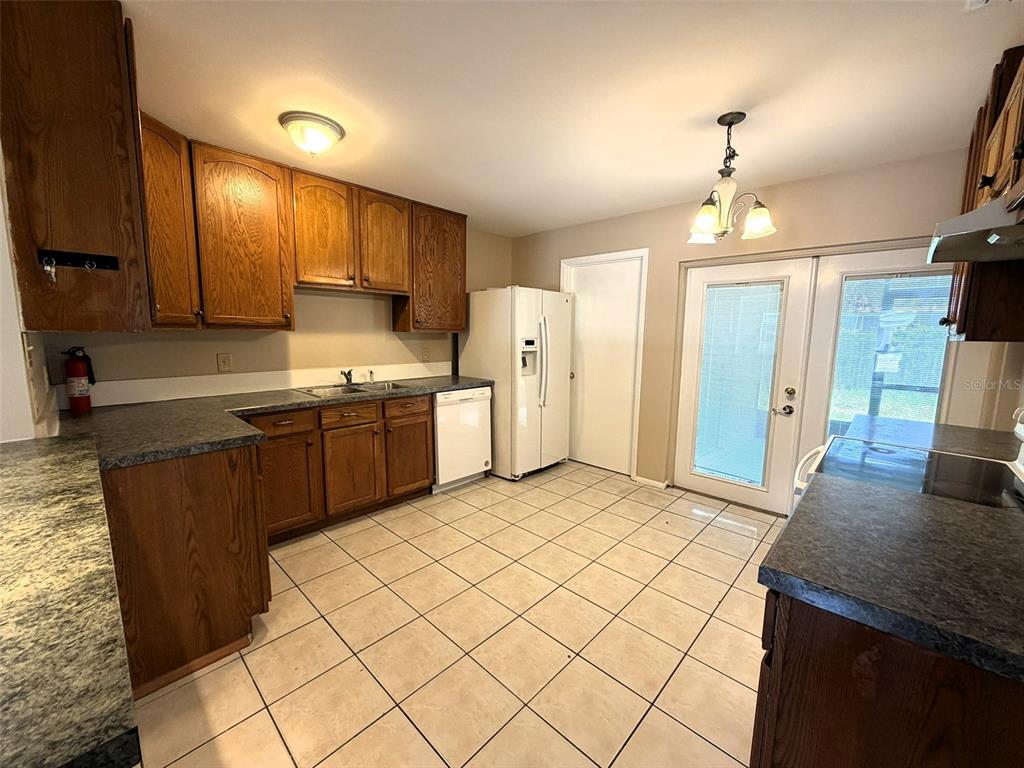 A kitchen features wood cabinets, dark countertops, tile flooring, and a white refrigerator — 8103 PUFFIN DRIVE, ORLANDO, FL