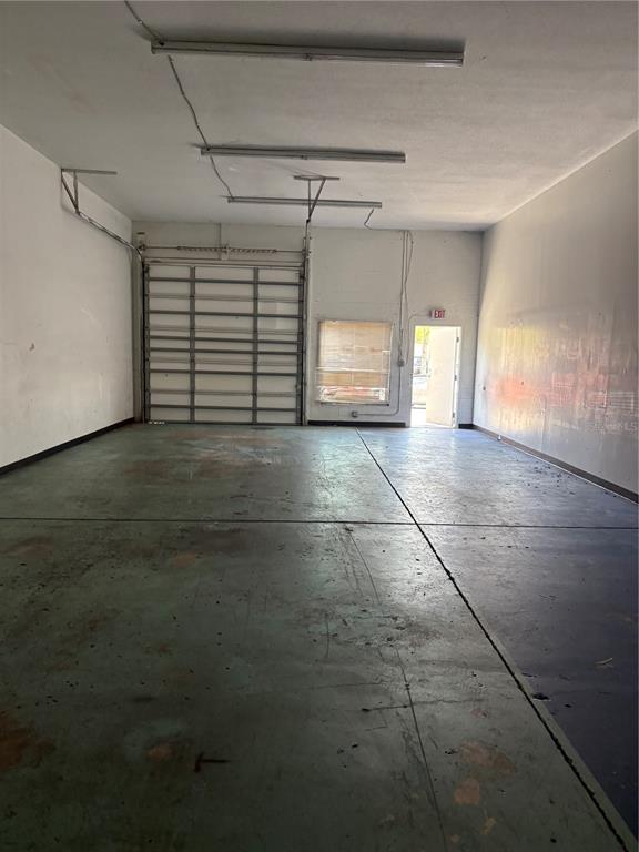An empty industrial warehouse space features a roll-up garage door, concrete floors, and fluorescent lighting — 19800 VETERANS BOULEVARD UNIT E4, PORT CHARLOTTE, FL