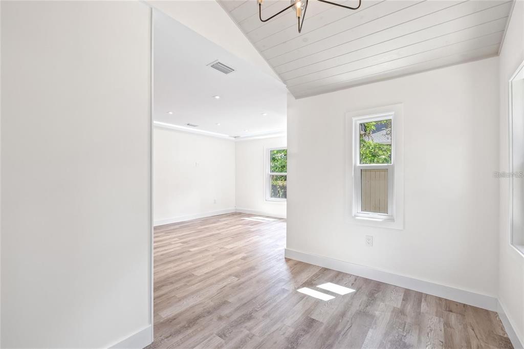An interior view shows a room with light wood flooring, white walls, and a vaulted ceiling — 6907 20TH STREET, TAMPA, FL