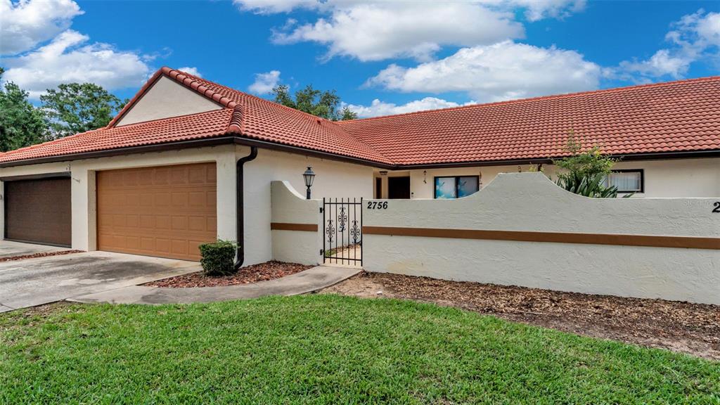 A single-story house with a red tile roof, a garage, and a gated courtyard entrance — 2756 DEL CASA COURT UNIT 18, AVON PARK, FL