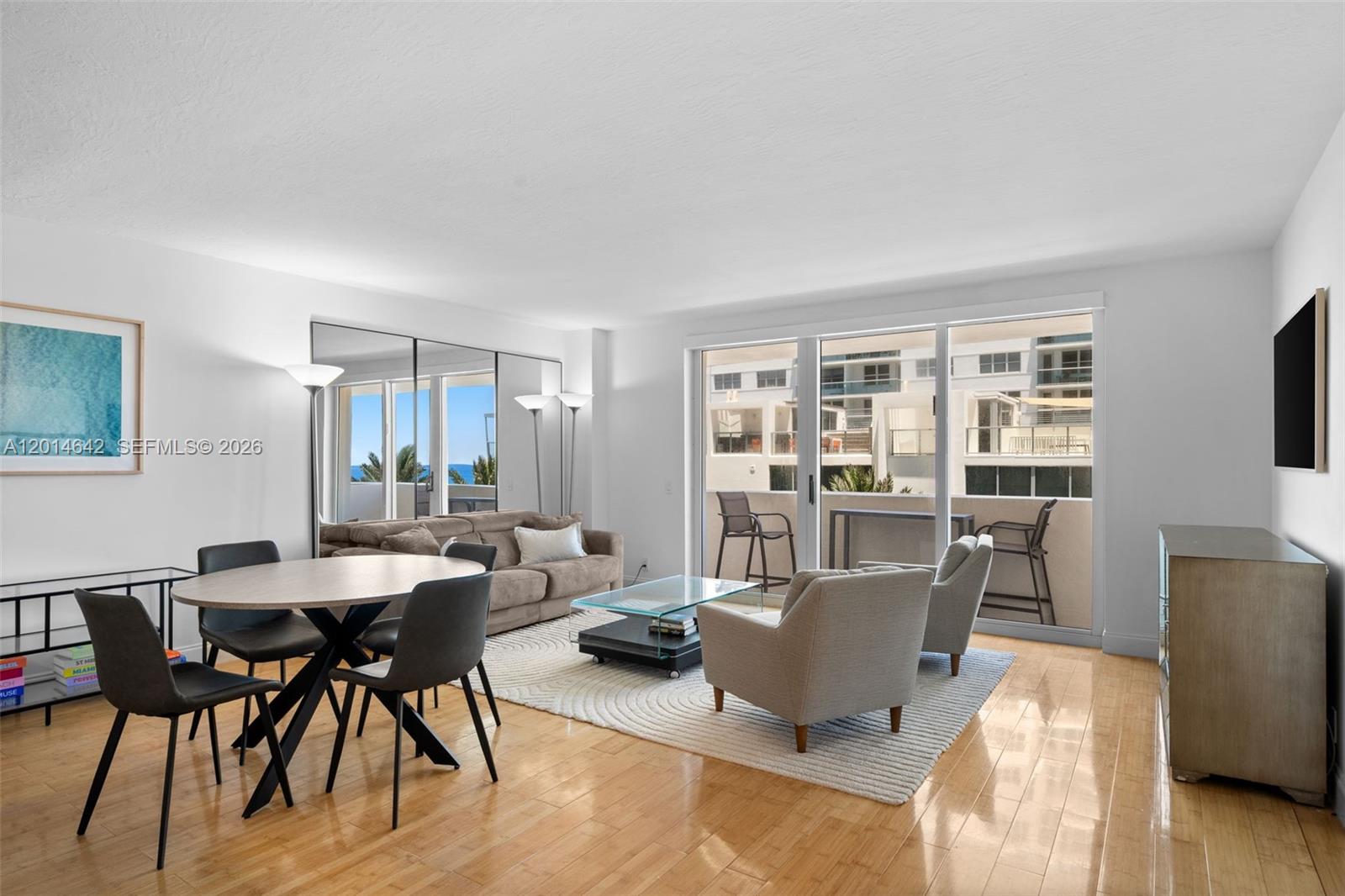 A bright living and dining area features hardwood floors, a balcony, and modern furniture — 9499 Collins Ave # 403, Surfside FL 33154, SURFSIDE, FL