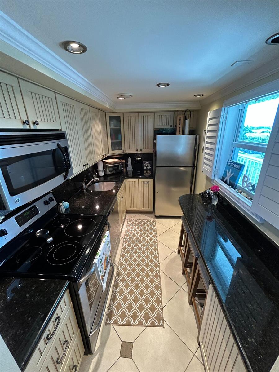 A galley kitchen features white cabinets, black granite countertops, stainless steel appliances, and tile flooring — 2829 Florida Boulevard # 502, Delray Beach FL 33483, DELRAY BEACH, FL
