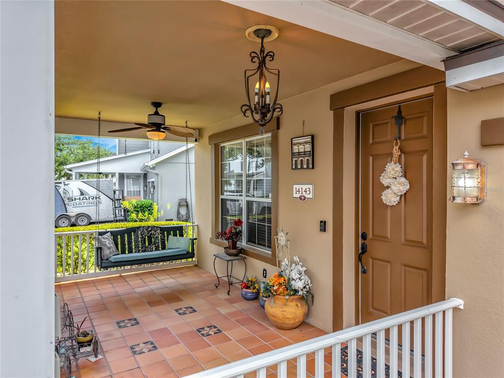 A covered front porch features a hanging bench, tiled flooring, and a brown front door — 14143 LAKE LIVE OAK DRIVE, ORLANDO, FL