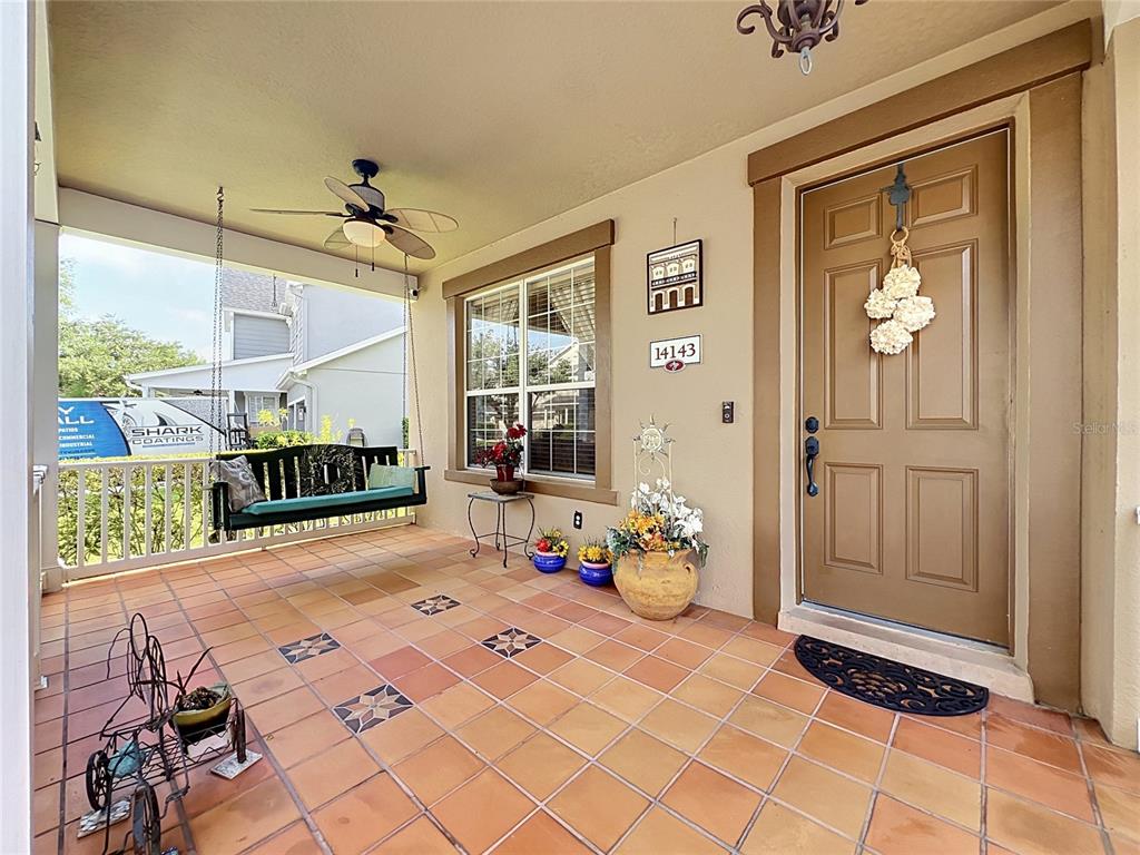 A covered front porch features a hanging bench, tiled floor, and a brown front door — 14143 LAKE LIVE OAK DRIVE, ORLANDO, FL