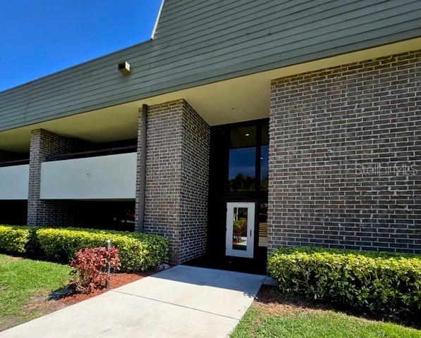 A brick building exterior features a concrete walkway leading to a glass-paned entrance door — 36750 US HIGHWAY 19 N UNIT 4-107, PALM HARBOR, FL