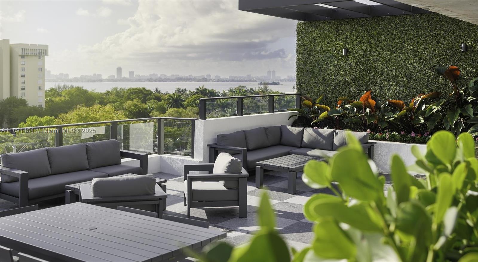 A furnished outdoor terrace features gray lounge seating, a dining table, and a green wall — 11200 Biscayne Blvd # A1, Miami FL 33181, MIAMI, FL