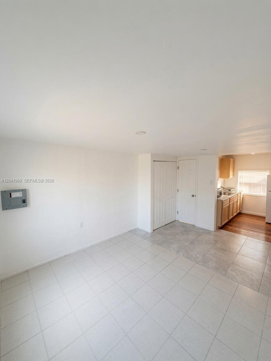 An interior view shows a tiled room with a white wall, a breaker panel, and a kitchen — 1340 Peri St # U, Opa-Locka FL 33054, OPA-LOCKA, FL