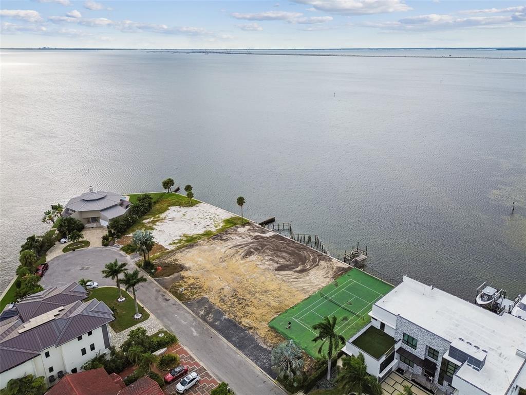 An aerial view shows a vacant waterfront lot with a tennis court next to houses — 5031 W SAN MIGUEL STREET, TAMPA, FL