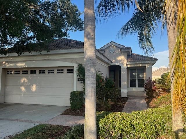 A single-story house with a two-car garage, a tiled roof, and a palm tree out front — 6517 TAILFEATHER WAY, BRADENTON, FL