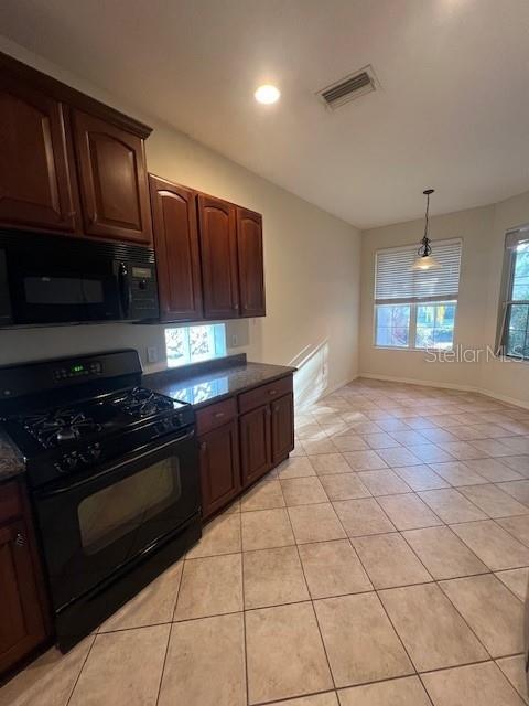 A kitchen with dark wood cabinets, black appliances, and tile flooring leads to a dining area — 6517 TAILFEATHER WAY, BRADENTON, FL