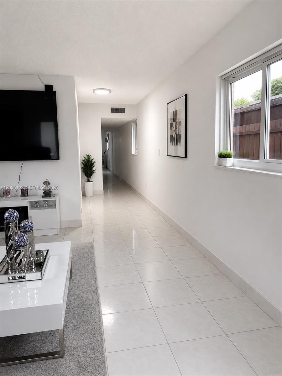 A bright living room features white tile floors, a wall-mounted television, and a long hallway — 380 W 45th St, Hialeah FL 33012, HIALEAH, FL