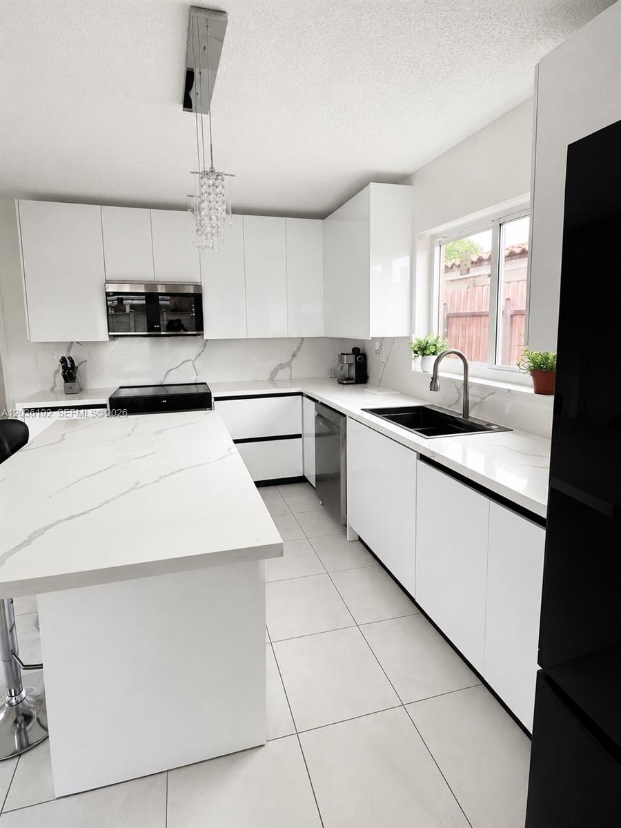 A modern kitchen features white flat-panel cabinets, a marble-patterned island, and a black sink — 380 W 45th St, Hialeah FL 33012, HIALEAH, FL