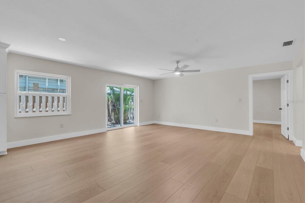 A bright, empty room features light wood flooring, white walls, a ceiling fan, and sliding doors — 714 3RD AVENUE NE, LARGO, FL