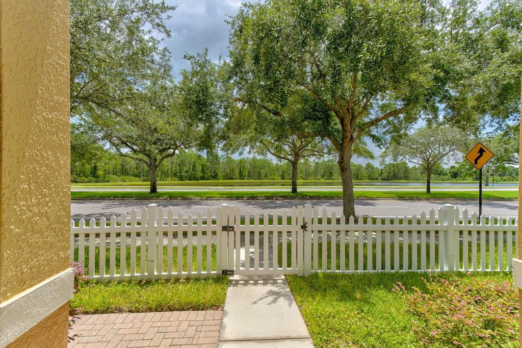 A white picket fence encloses a patio area overlooking a road, trees, and a pond — 2463 LACERTA DRIVE, ORLANDO, FL