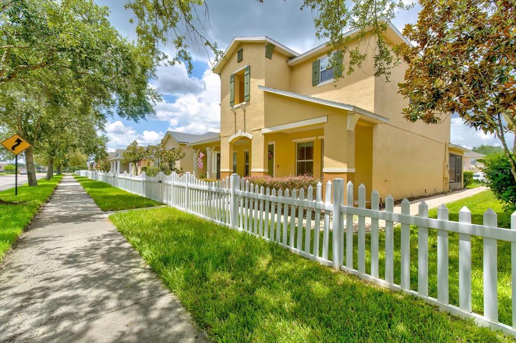 A two-story yellow house with a white picket fence and a sidewalk in the foreground — 2463 LACERTA DRIVE, ORLANDO, FL