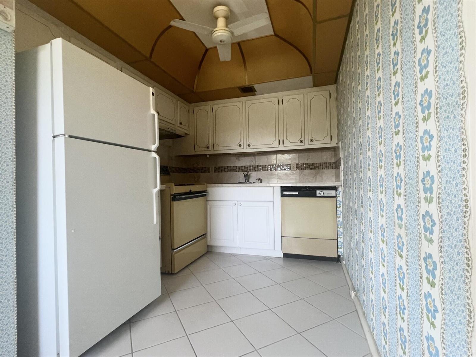 A small kitchen features white cabinets, beige appliances, a tiled floor, and floral wallpaper — 392 Grantham F # 392, Deerfield Beach FL 33442, DEERFIELD BEACH, FL