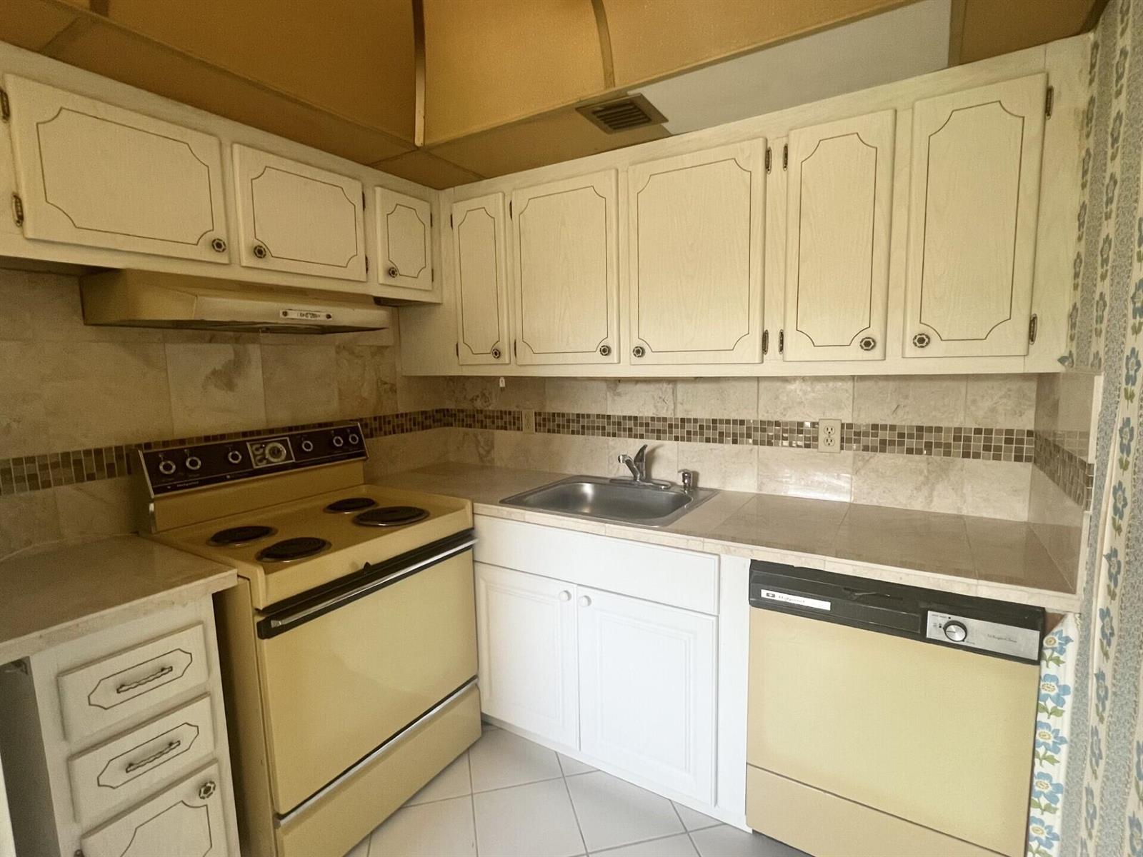 A kitchen features off-white cabinets, a yellow stove and dishwasher, and a tiled backsplash — 392 Grantham F # 392, Deerfield Beach FL 33442, DEERFIELD BEACH, FL