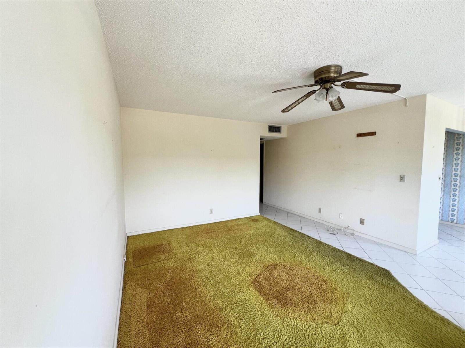 An empty room features green wall-to-wall carpeting, white tile flooring, and a ceiling fan — 392 Grantham F # 392, Deerfield Beach FL 33442, DEERFIELD BEACH, FL