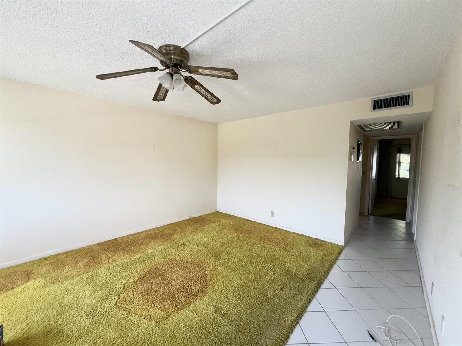 An empty room features green shag carpeting, a ceiling fan, and an adjacent tiled hallway — 392 Grantham F # 392, Deerfield Beach FL 33442, DEERFIELD BEACH, FL