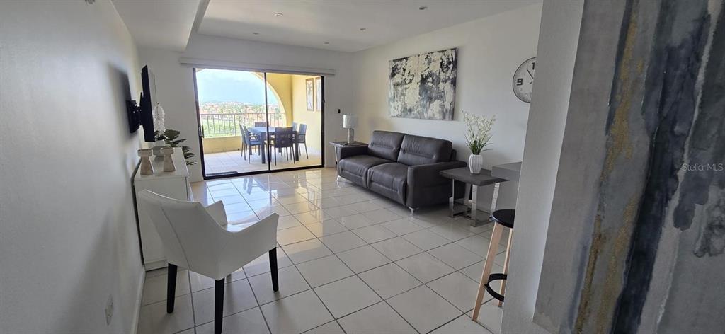 A living room with tile floors, a dark leather sofa, and a balcony with outdoor seating — Palmas del Mar PALMANOVA UNIT 321, HUMACAO, PR