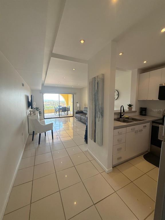A kitchen with white cabinets opens into a living area with tile floors and balcony access — Palmas del Mar PALMANOVA UNIT 321, HUMACAO, PR