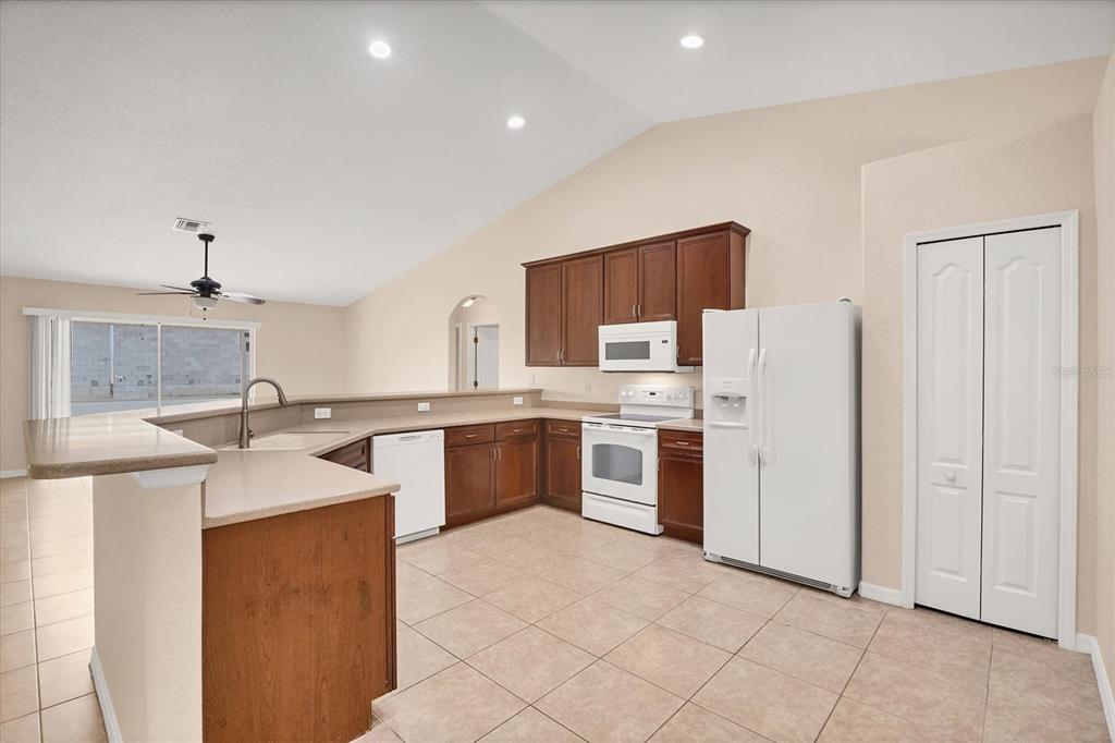 A kitchen with brown cabinets, white appliances, a breakfast bar, and light-colored tile flooring — 15117 LYNEBURG AVENUE, PORT CHARLOTTE, FL